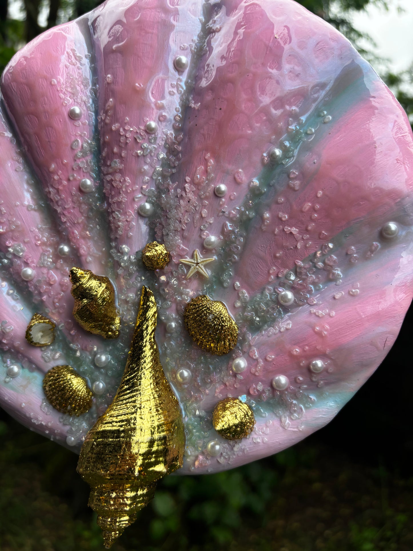 Textured art painting with pink shell-like surface, adorned with gold shells, and pearls on a natural plants background